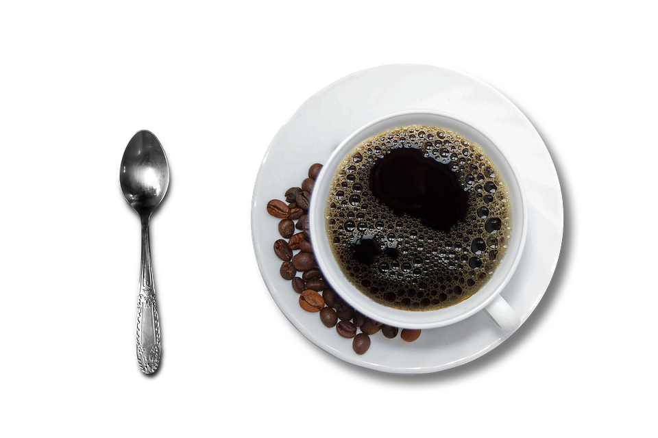 A cup of coffee together with some roasted coffee beans and a teaspoon.