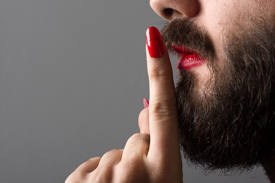 A close up of a bearded male's face, with red lipstick and a hand with fake nails and red nail polish.