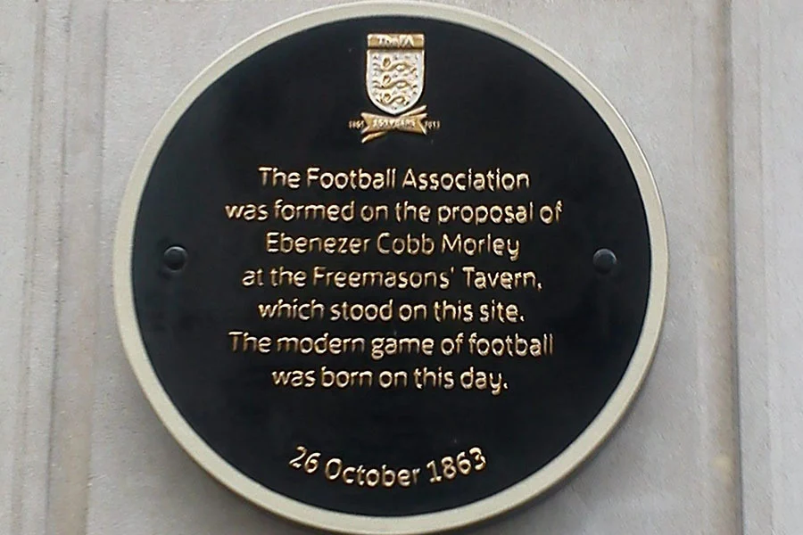 Round metal plaque with the words 'The Football Association was formed on the proposal of Ebernezer Cobb Morley at the Freemason's Tavern, which stood on this site. The modern game of football was born on this day. 26 October 1863'