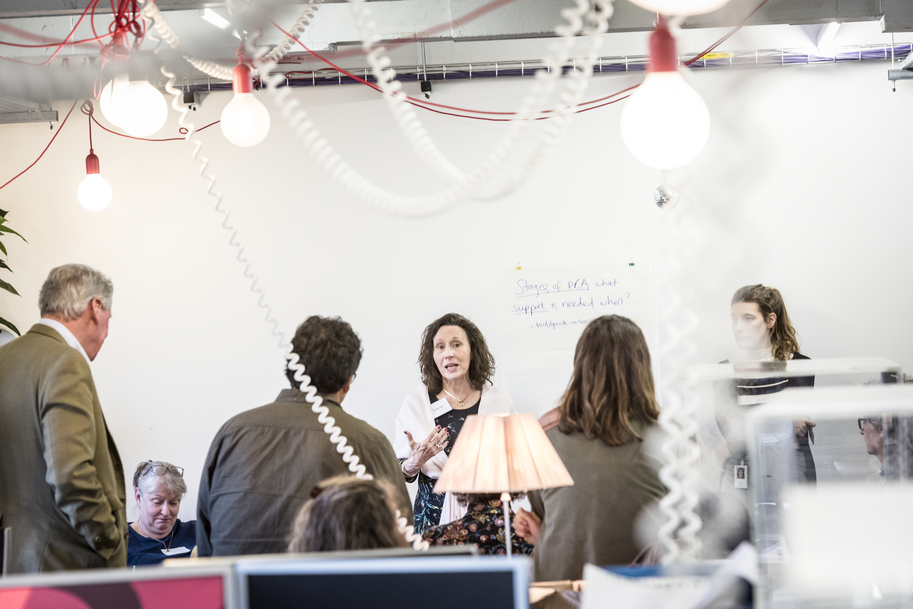 Photograph of a group of people, listening to a person speaking