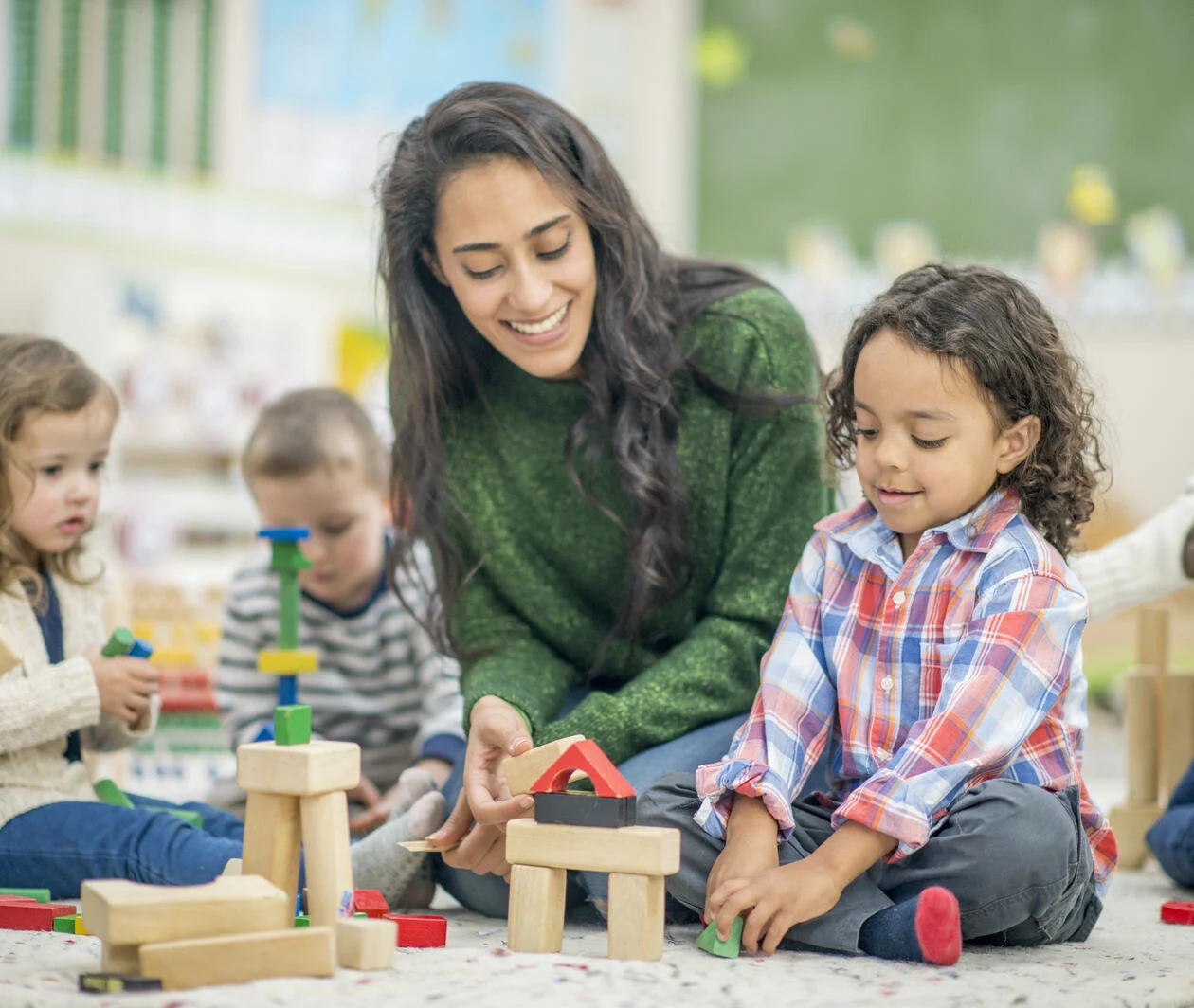 Learning facilitator helping children build a house out of wooden building blocks