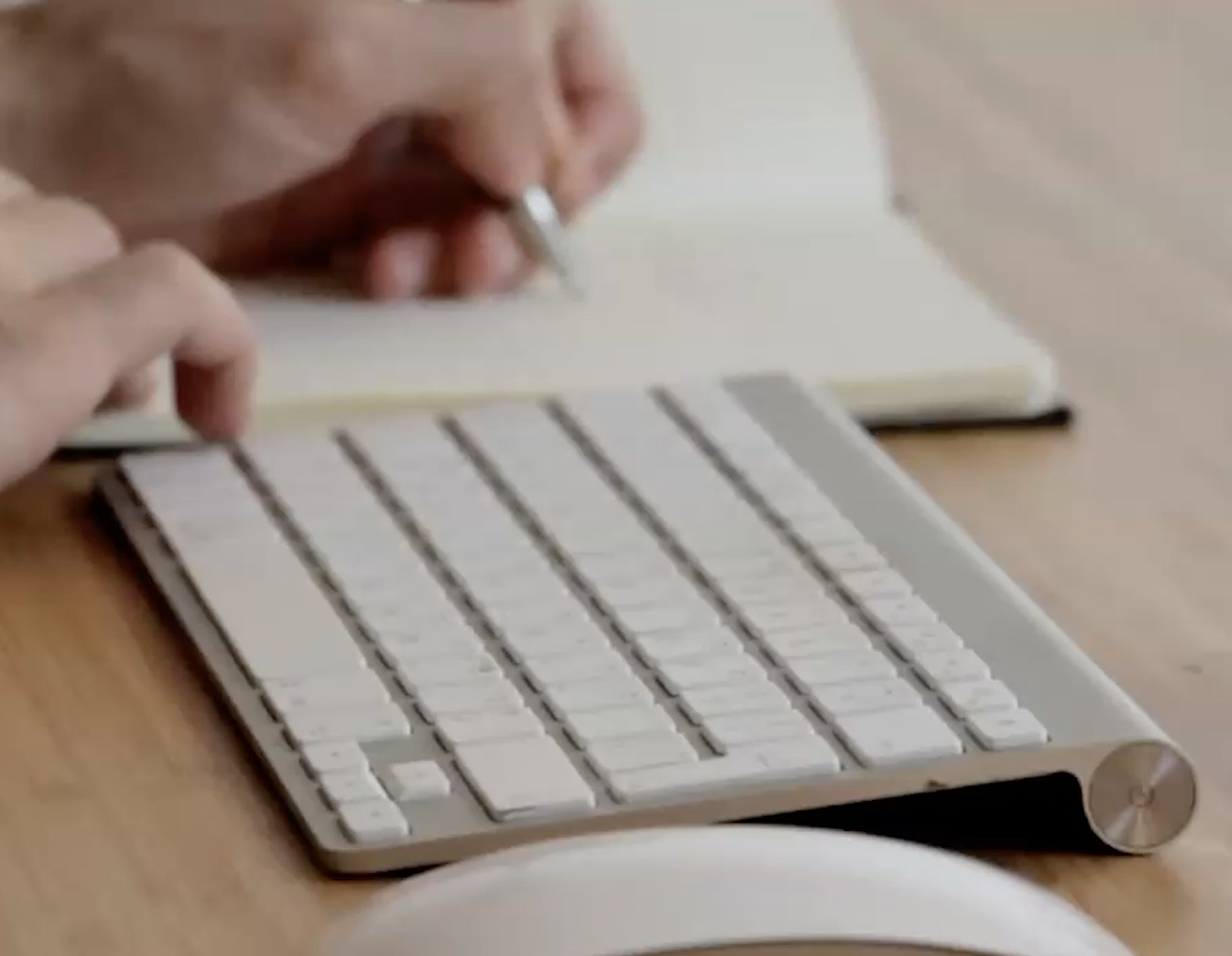 photogaph of a person writing beside a computer keyboard