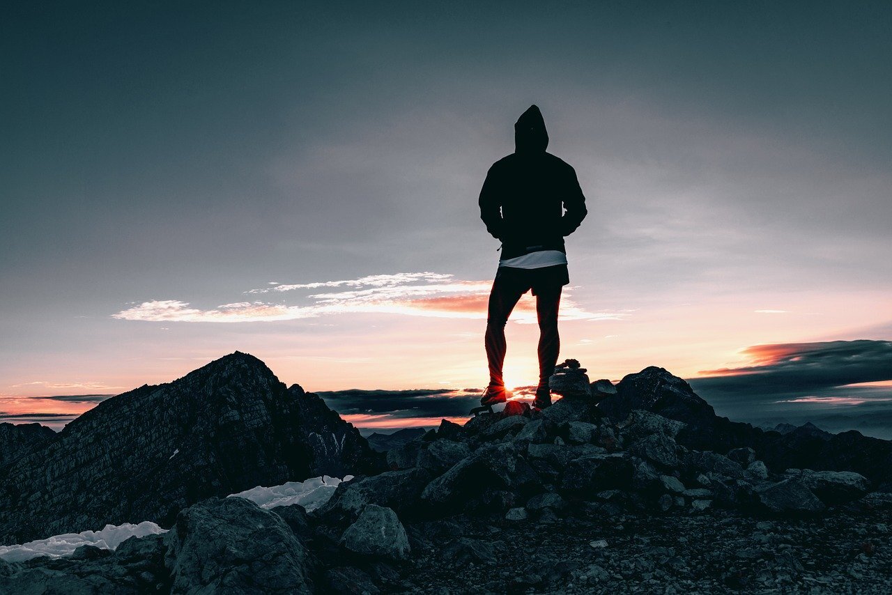 A mountain runner looks out from a peak at sunrise