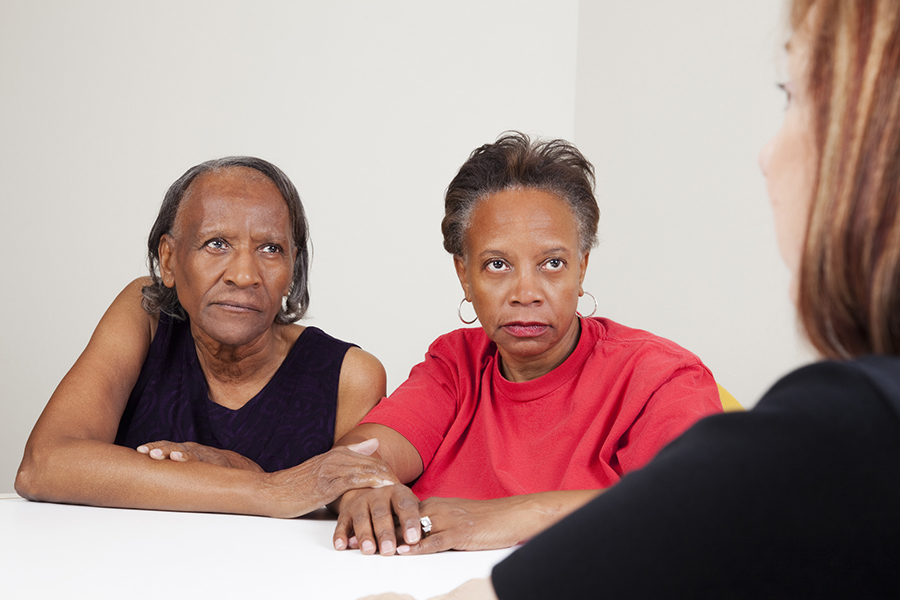 Serious african-american mother and daughter talking with a care worker