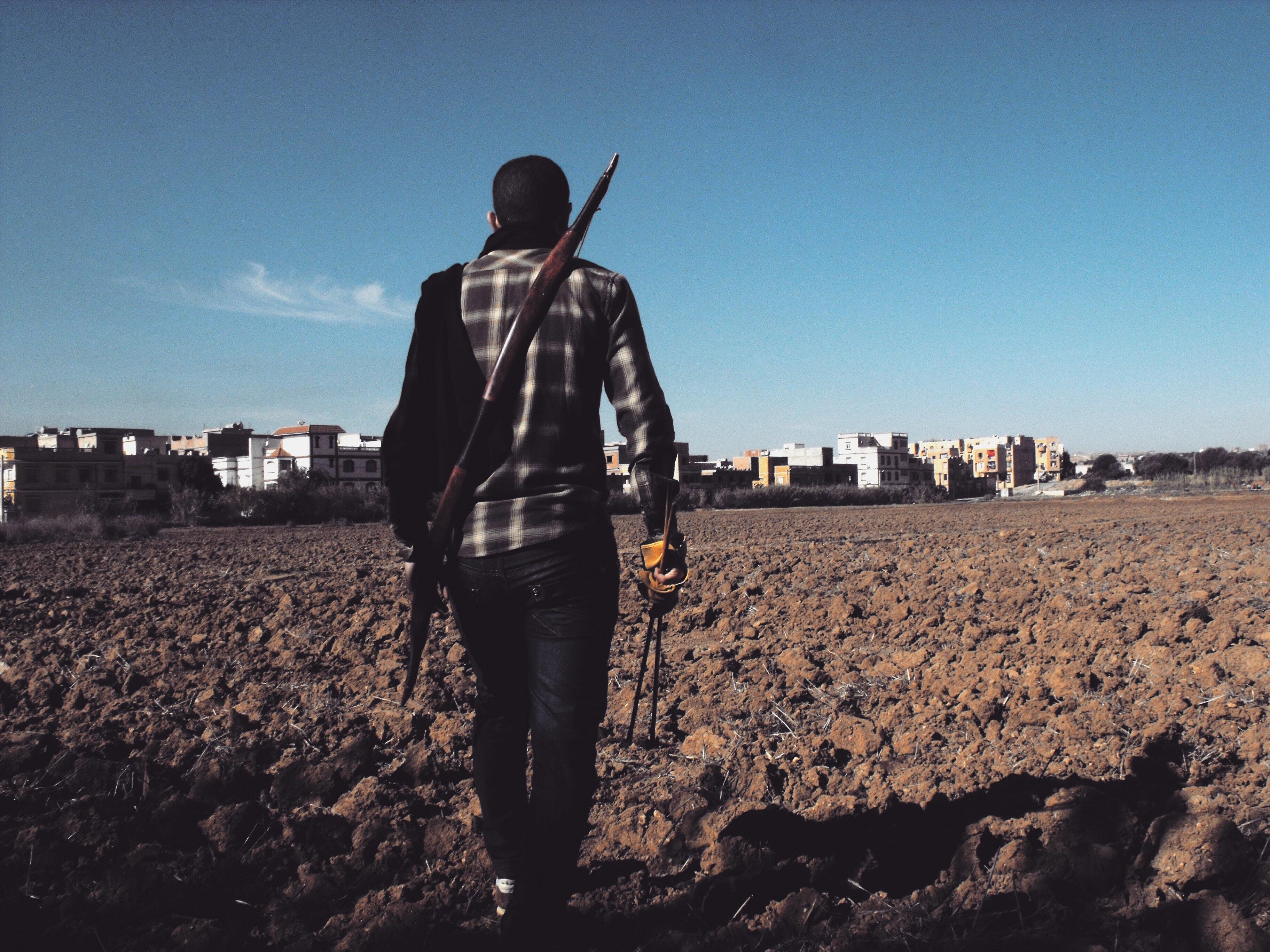 a man walking towards the horizon holding some arrows.