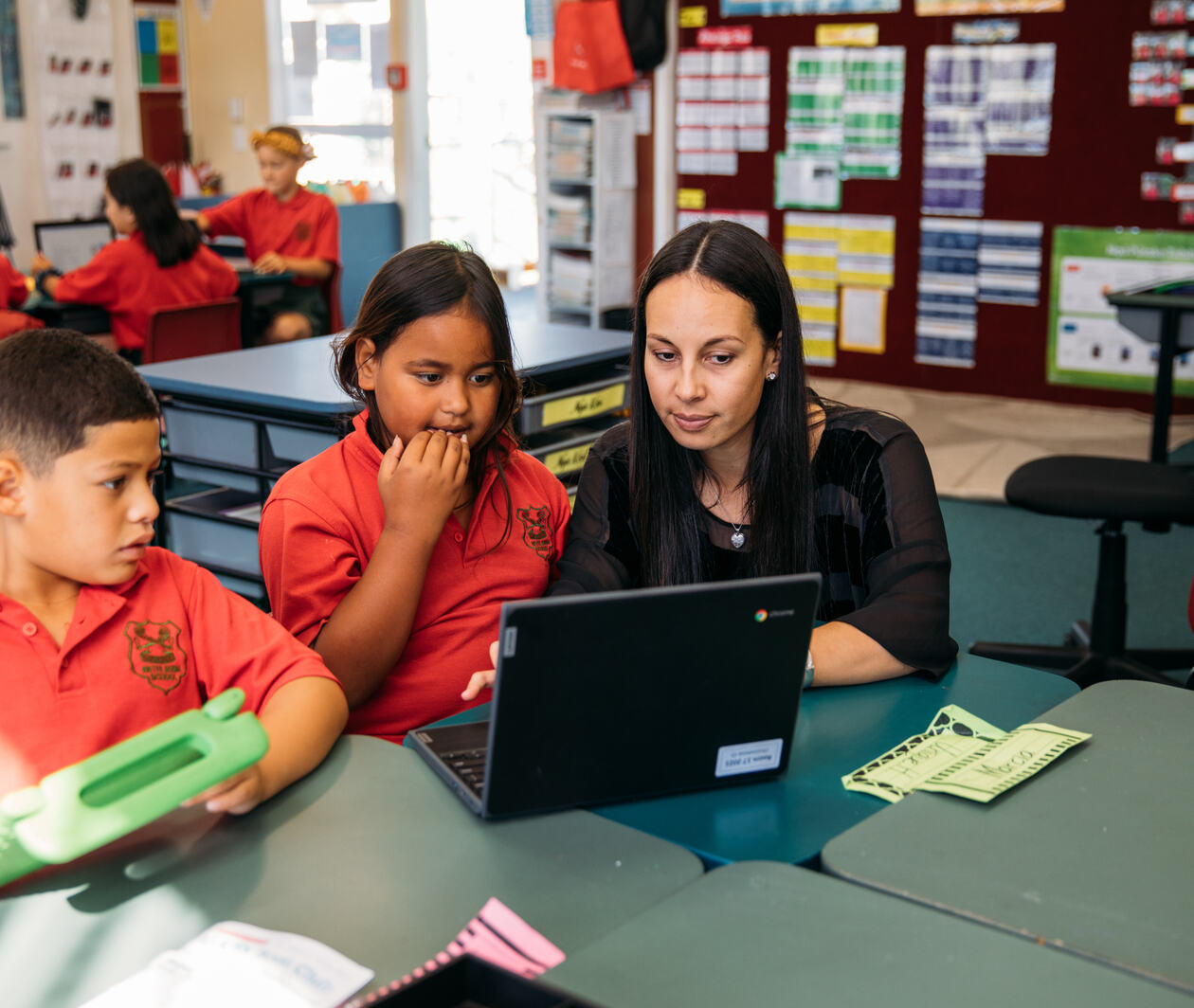 A teacher helping her students work on a laptop