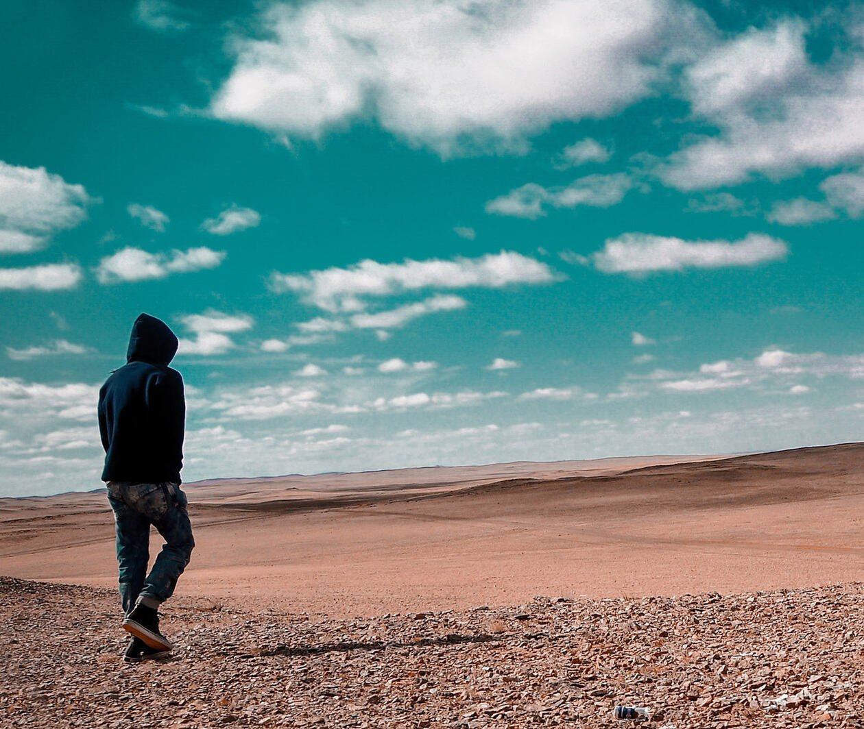 Person standing alone in a rocky desert wearing a hoodie and jeans