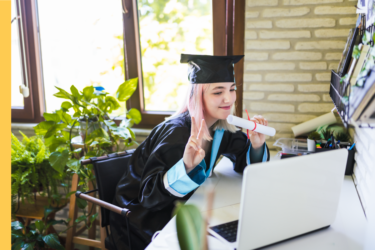 Woman in graduation cap and gown showing her diploma to a video call on her laptop