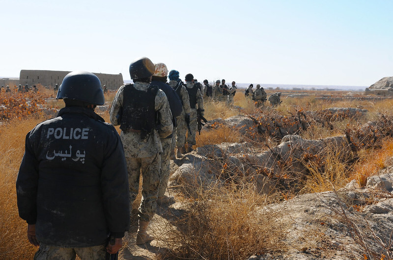 Afghan police and security forces walk through a grape field during a counternarcotics raid.