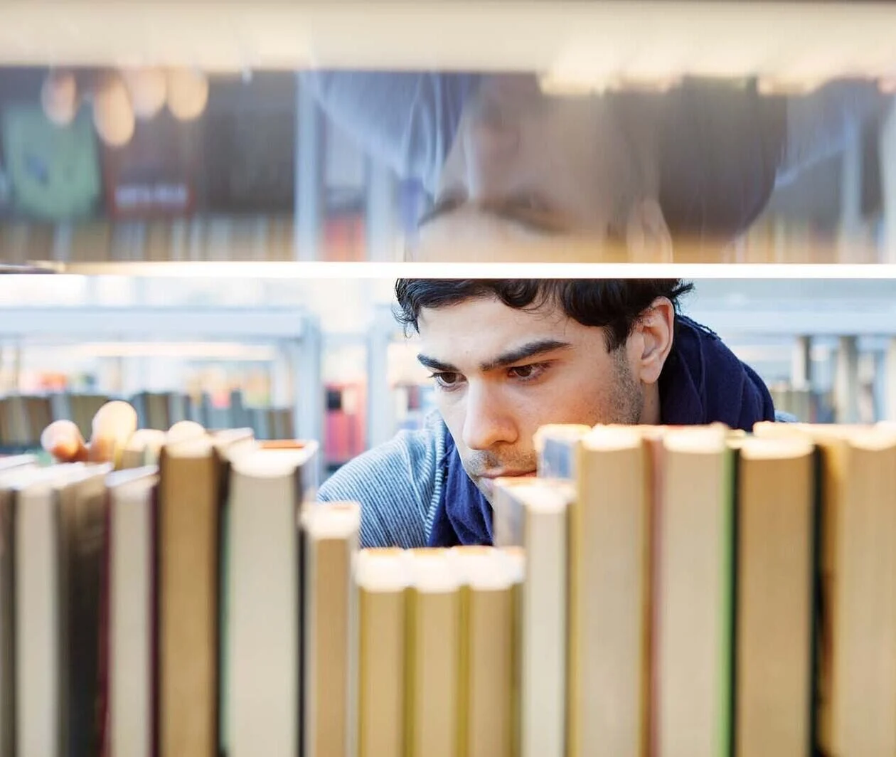 A man with dark hair looking intensely at a book shelf. 