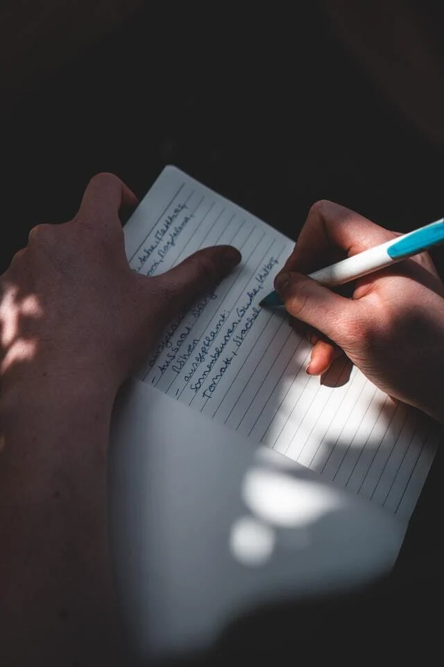 Person writing on white lined paper with a pen