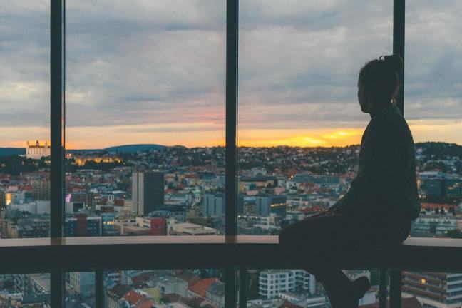 Woman looking out of a large window over a cityscape