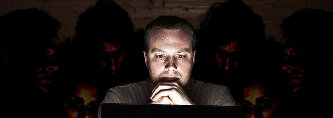A cyber security threat - a man looks at his laptop, while people snoop over his shoulder