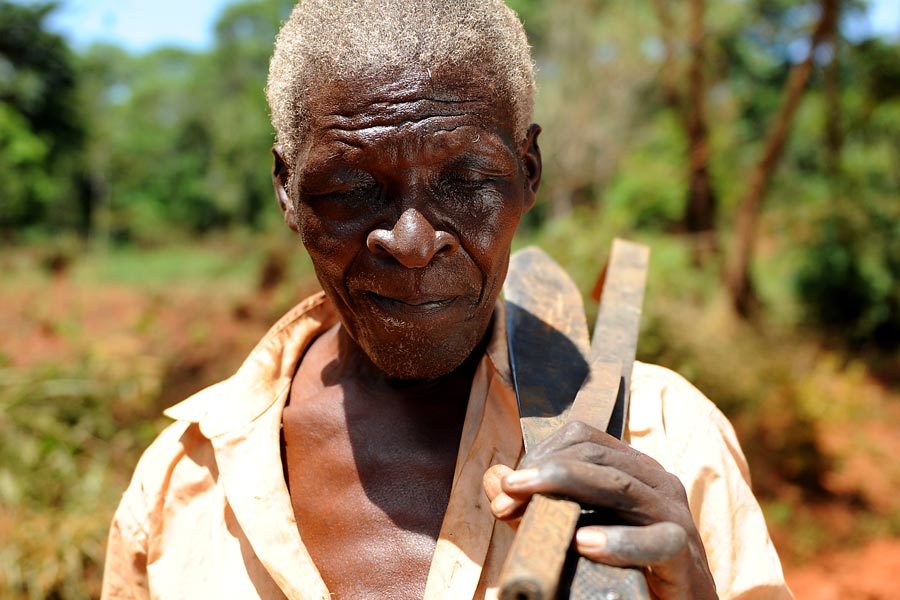 A visually impaired man carrying his farm tools.