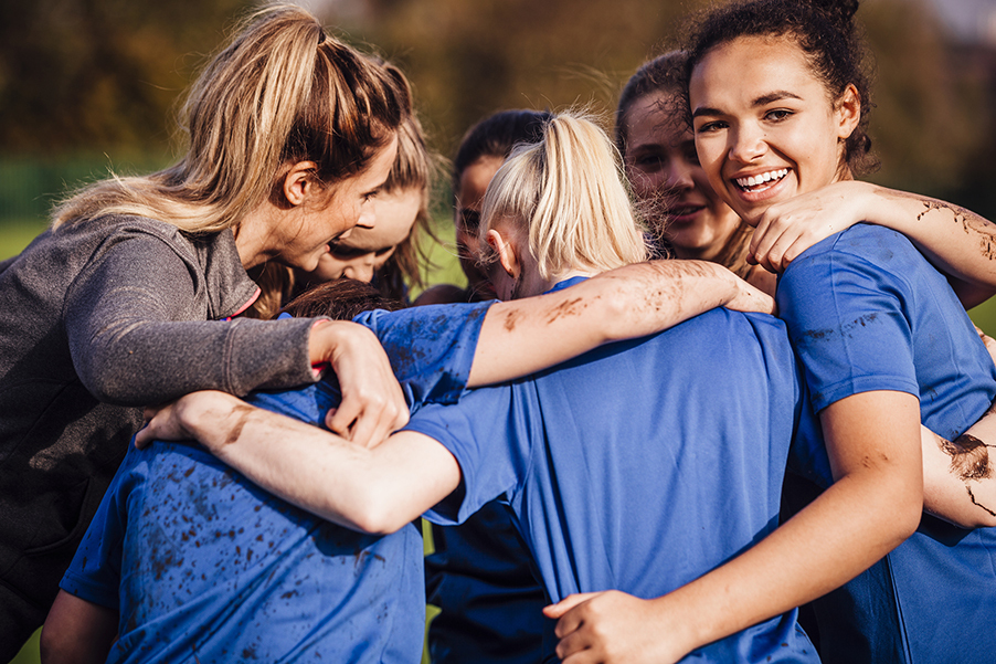 Female Rugby Players Together in a Huddle Young teenage girls smiles as she gathers around with her team mates for a chat during their rugby game