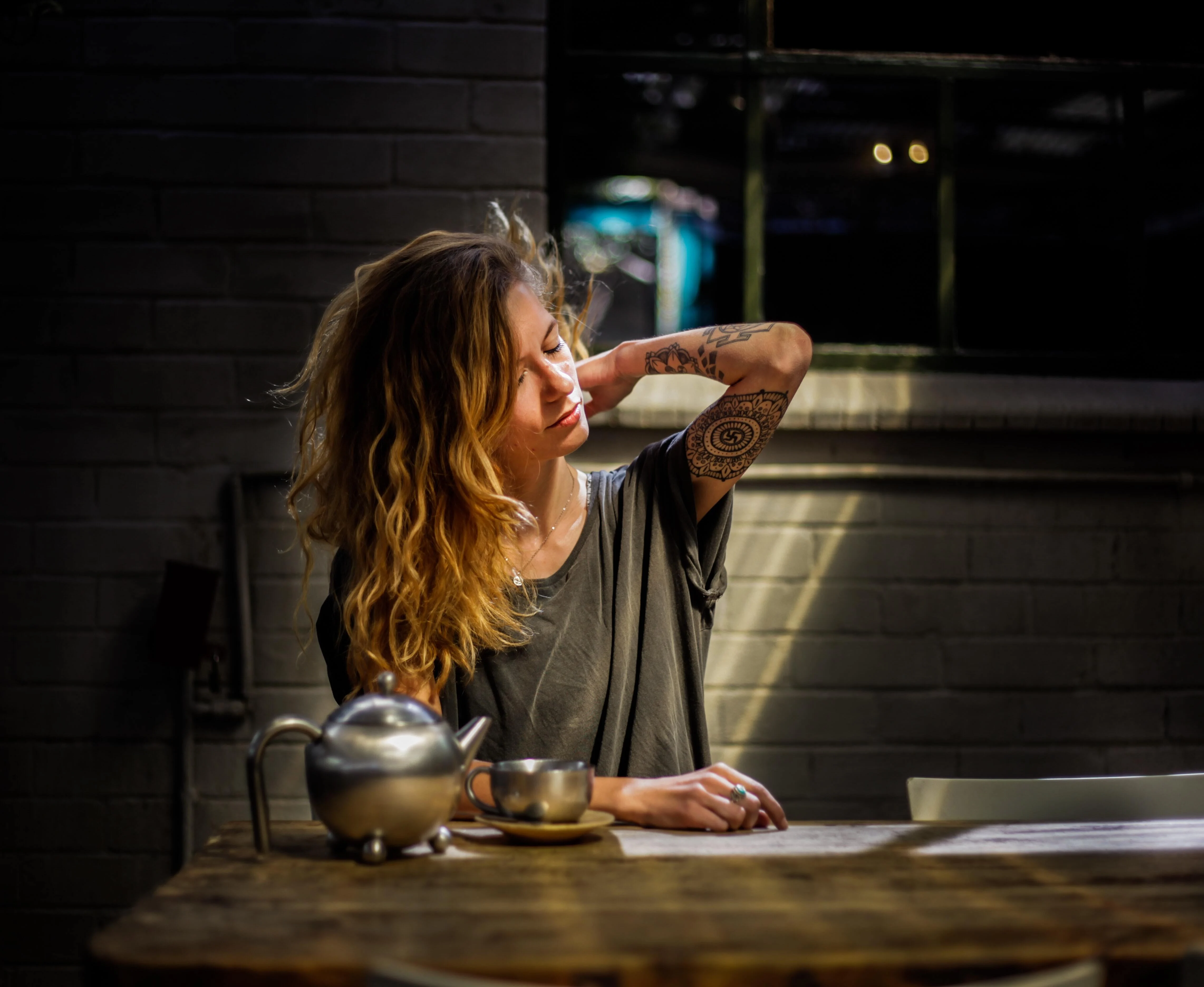 Tattooed lady rubbing her neck and drinking a pot of tea