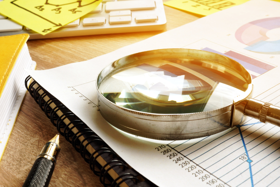 Magnifying glass on a financial report, next to a notebook and pen