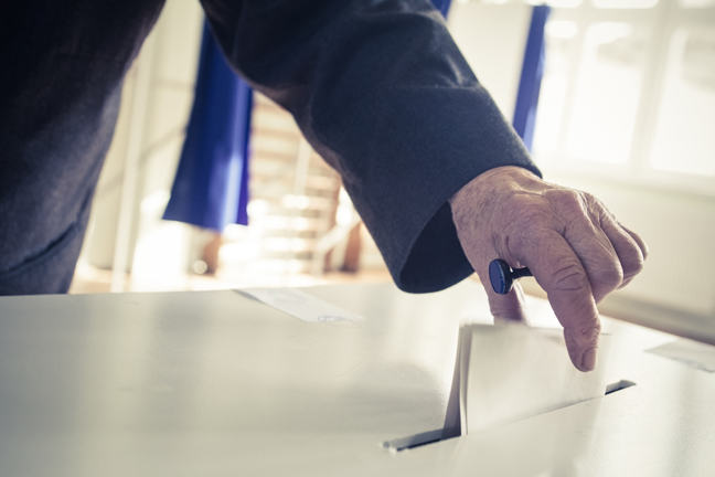 Photo of someone placing their voting paper into a voting box.