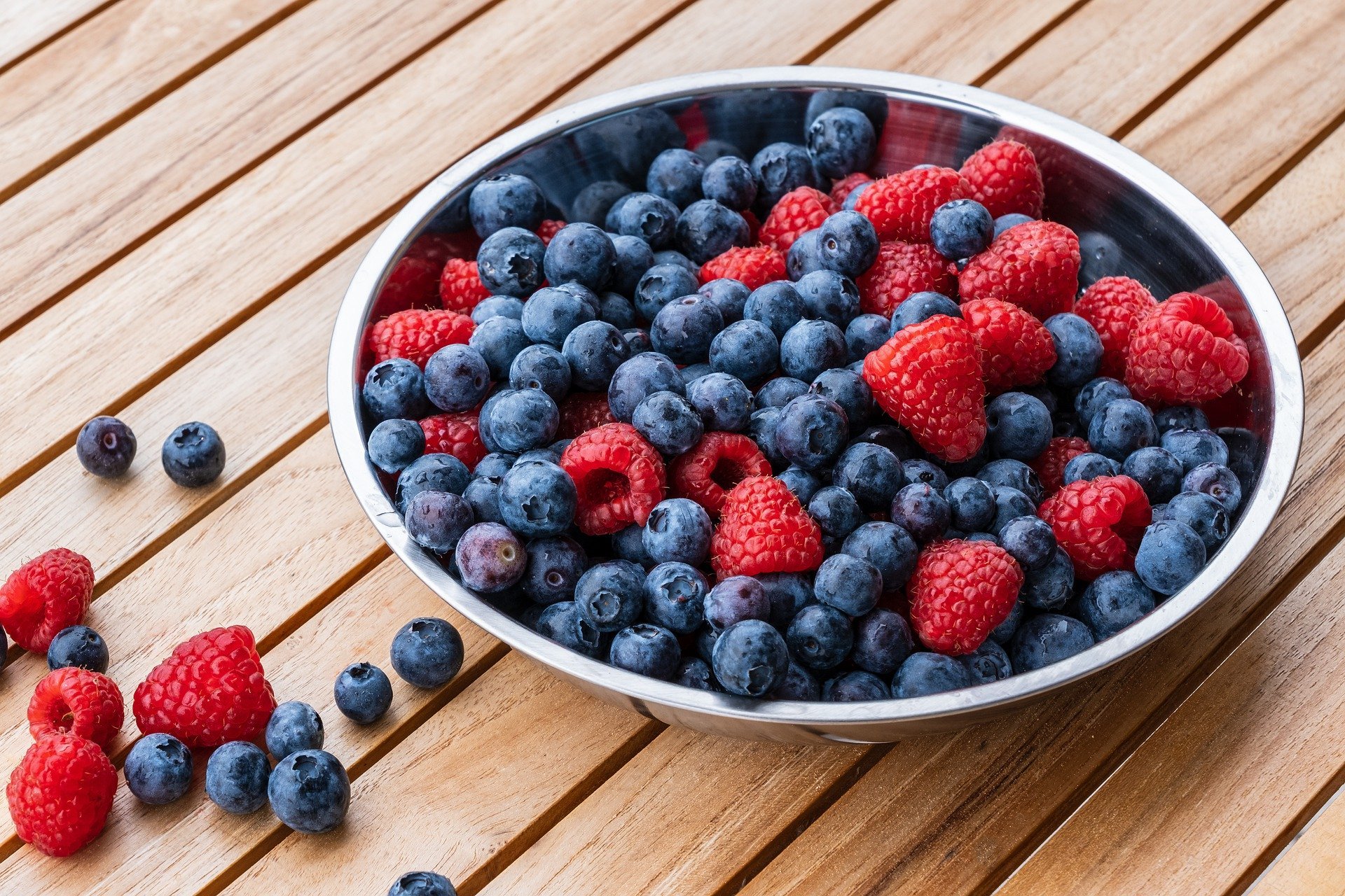 raspberries and strawberries in a metalic bowl on a wooden table