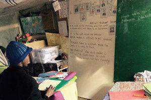 Two refugees, one male, one female sitting in a makeshift classroom looking at writing on a board