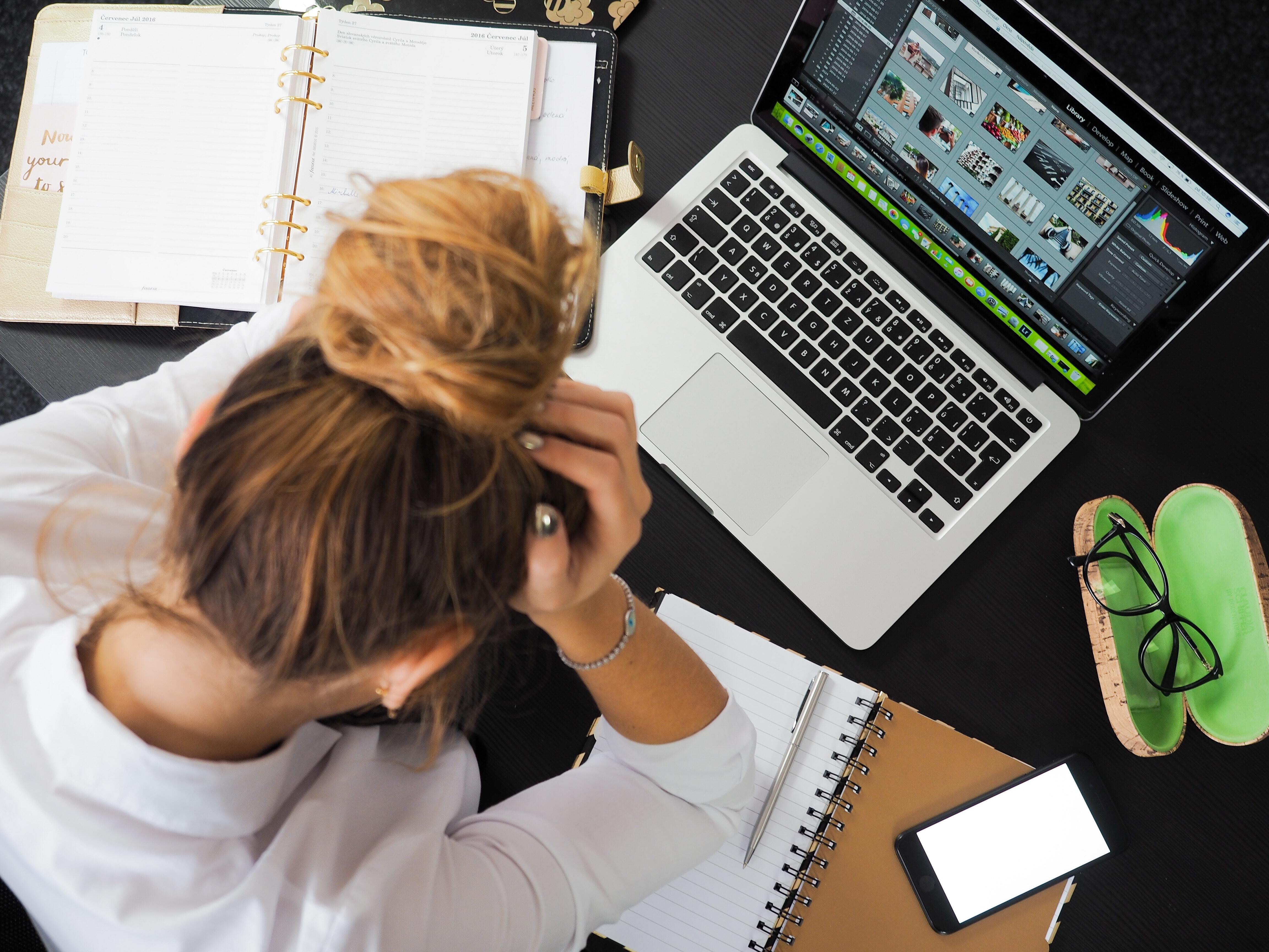 Woman sits in front of Macbook with head in hands