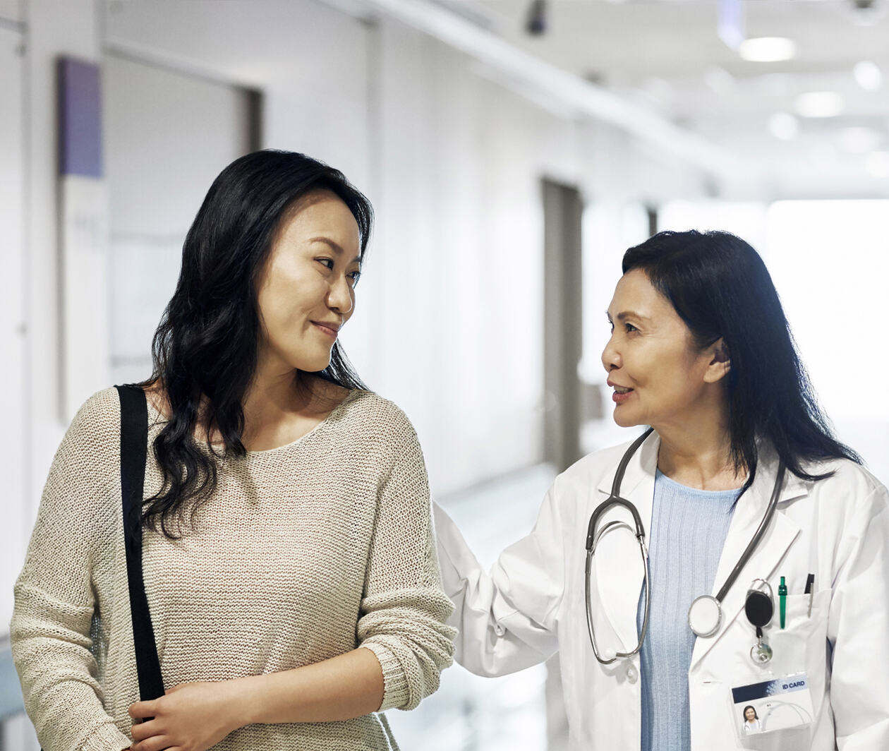 Smiling mature doctor talking to woman at a corridor in hospital.