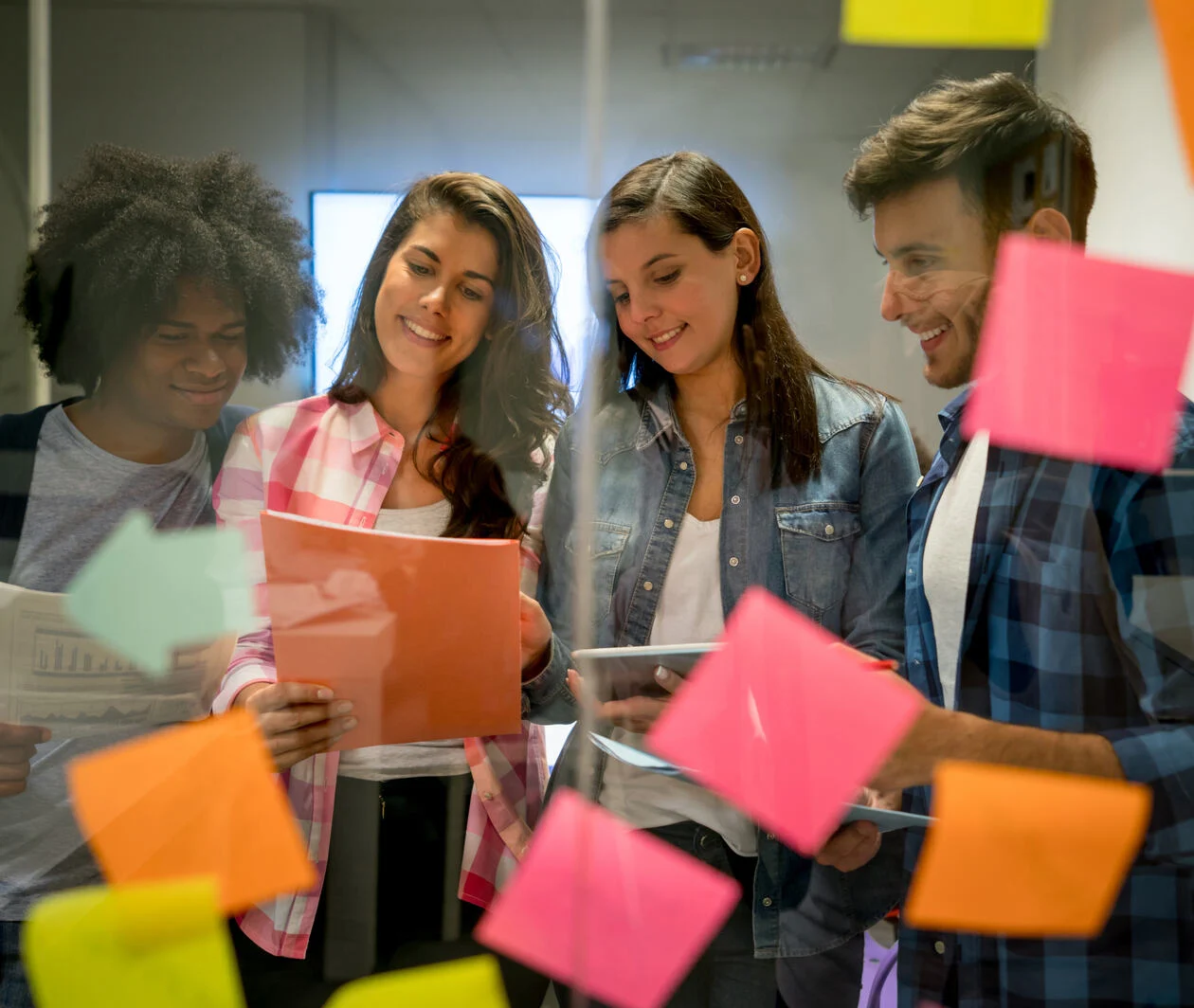 A group of people viewed through an office window that is covered in post it notes