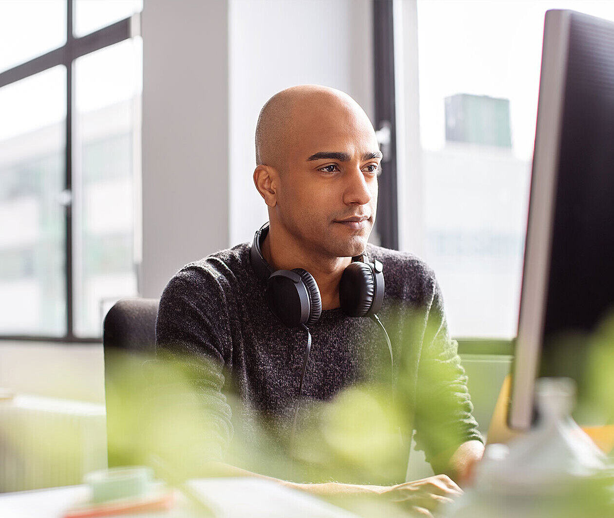 Person with headphones round their neck looking at a computer screen.