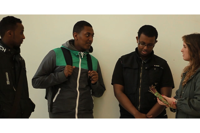 A still from the film 'Khat' shows the interviewer talking to three young men about their opinions of the substance. She holds a stick of Khat.