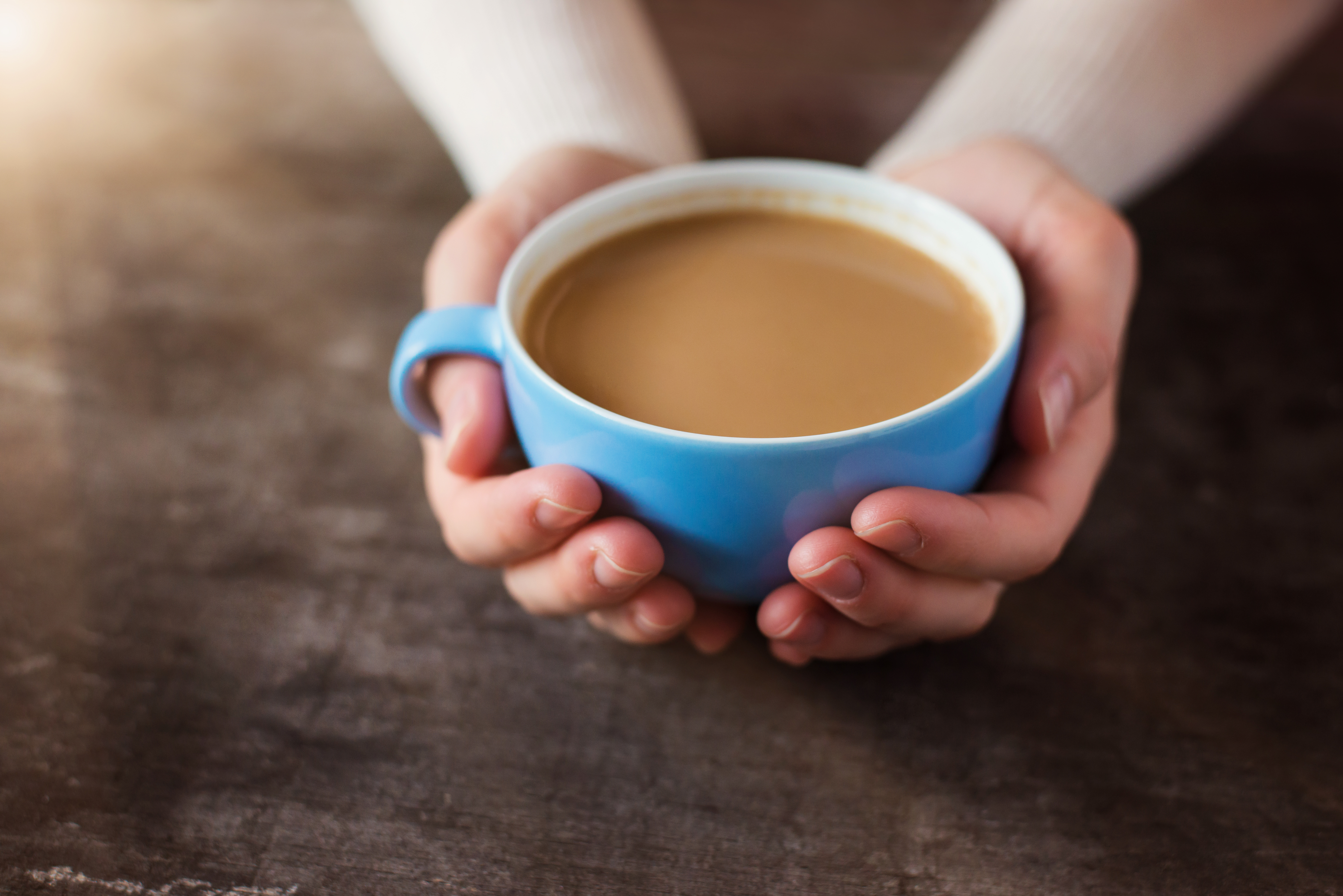 Unrecognizable woman holding a cup of coffee on a wooden table background