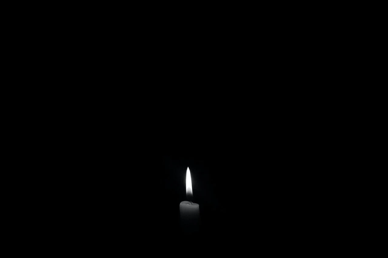 In black and white, and utter darkness, a lit candle sits alone with only its flame penetrating the darkness..