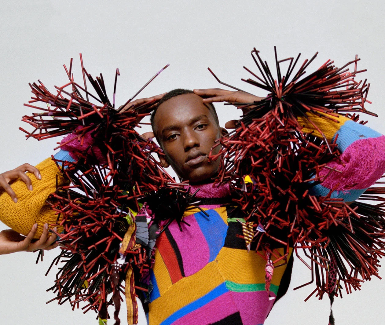 A Fashion industry model poses wearing a colourful outfit with tassel sleeves. 