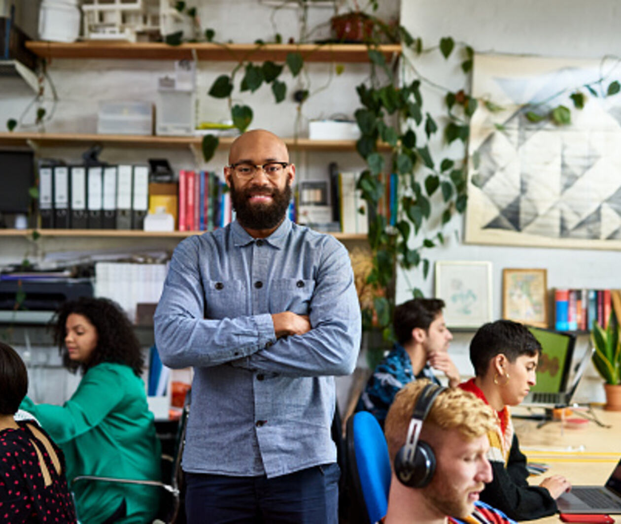 Entrepreneur in busy office smiling at camera, with plants and files in the background.