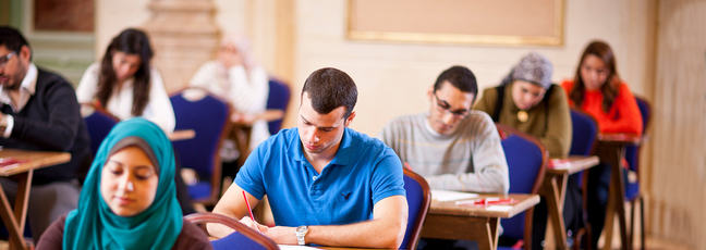 Students sitting t desks in an examination room.