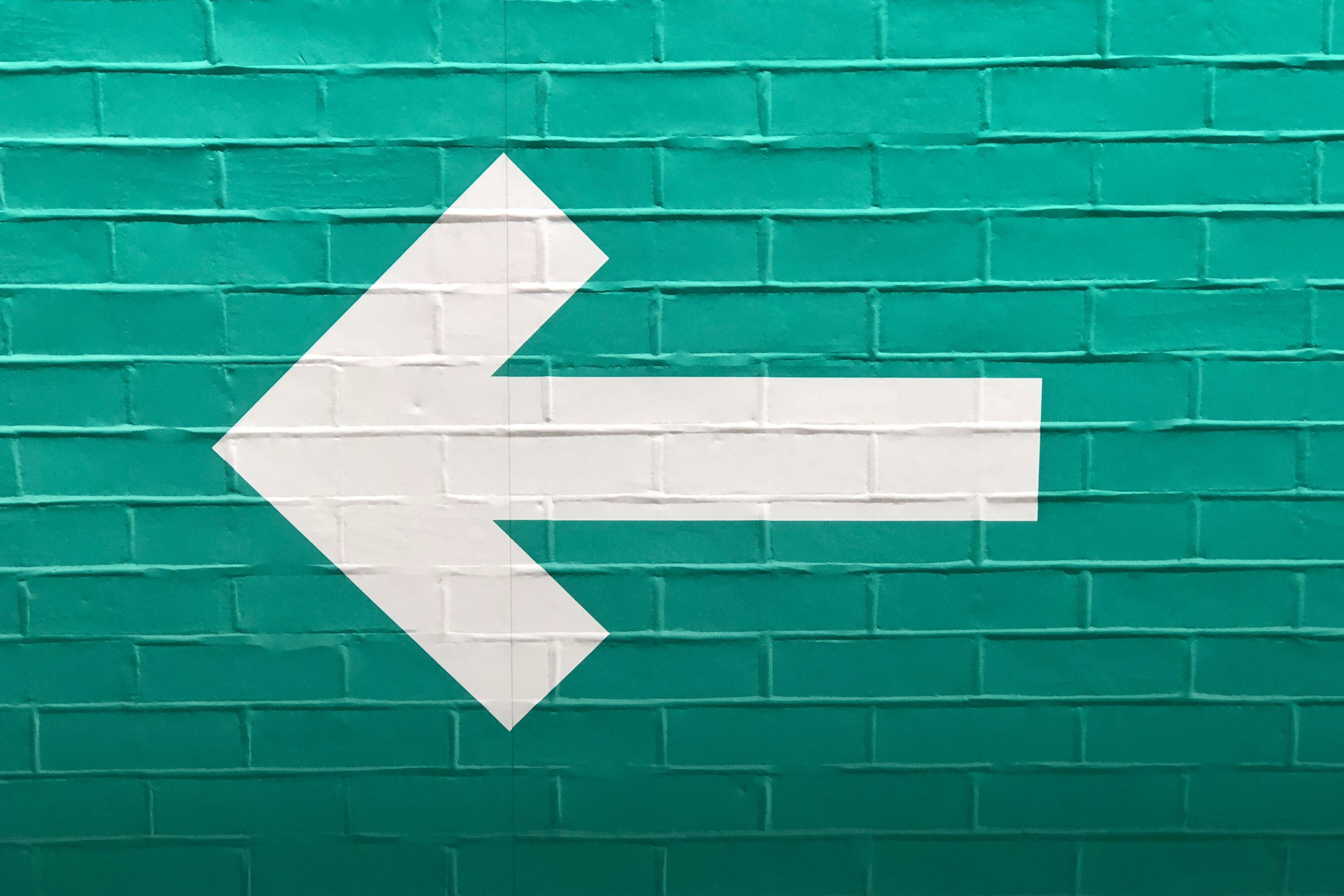 blue brick wall with white arrow pointing to the left painted over