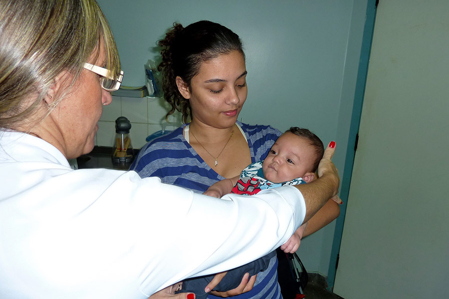 Therapist gently holds the back of an older baby's hed as he looks at her. He is cradled in his mother's arms