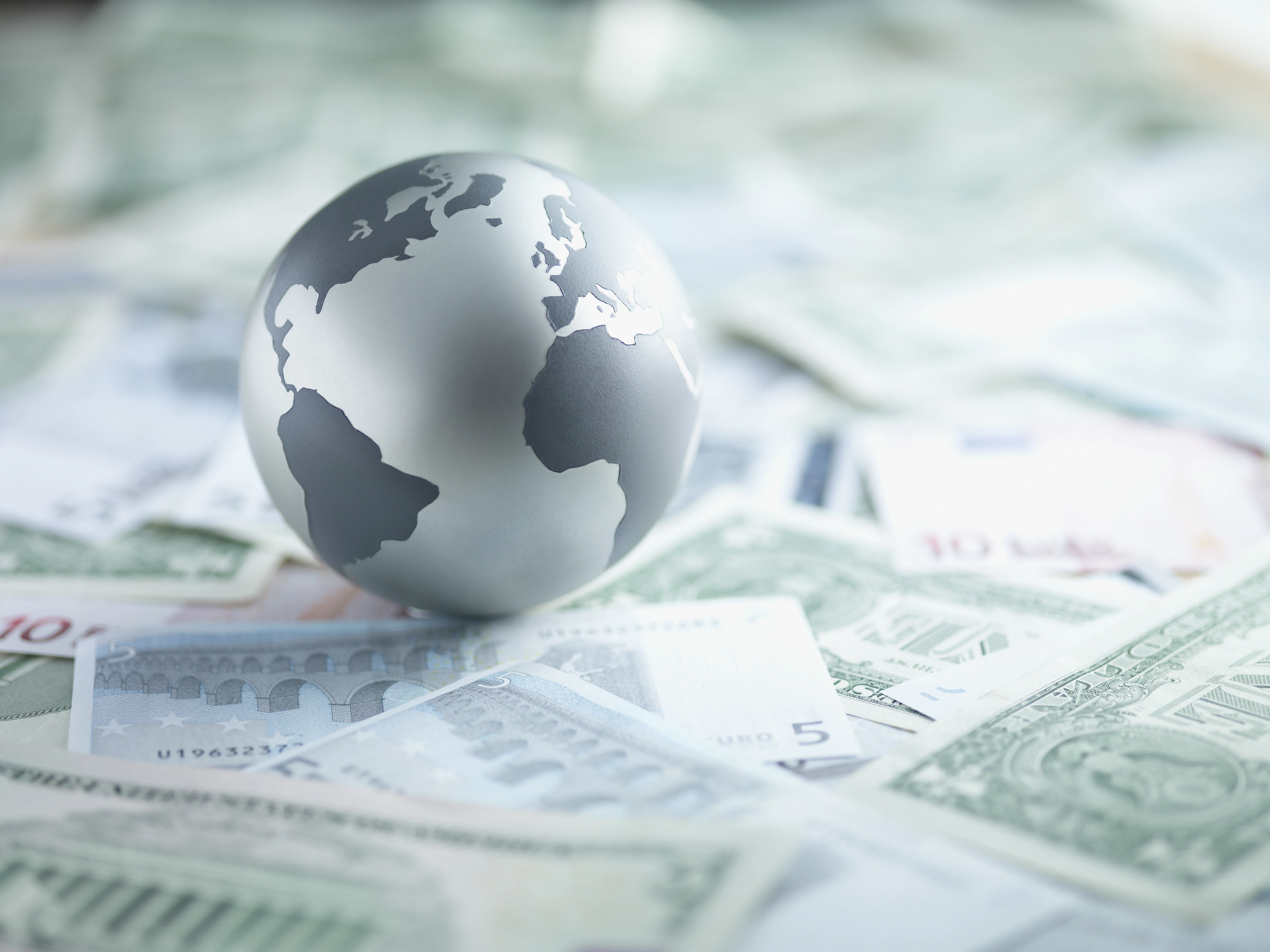 Paper globe resting on a large pile of paper currency.