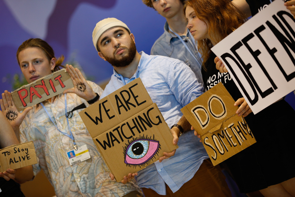 people holding placards that say 'we are watching' ' do something'.