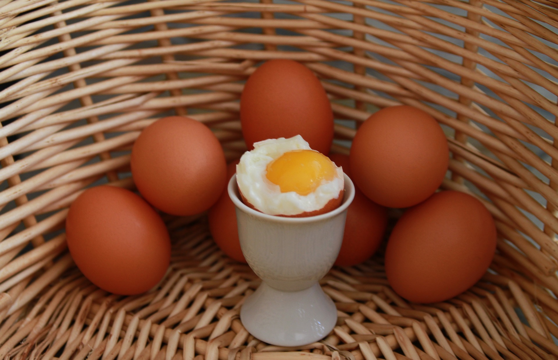 a soft boiled egg in a egg cup surrounded by other eggs in a basket