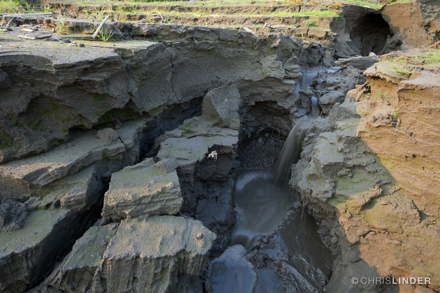 Deeply eroding soil, with a rivulet of water pouring down the middle.