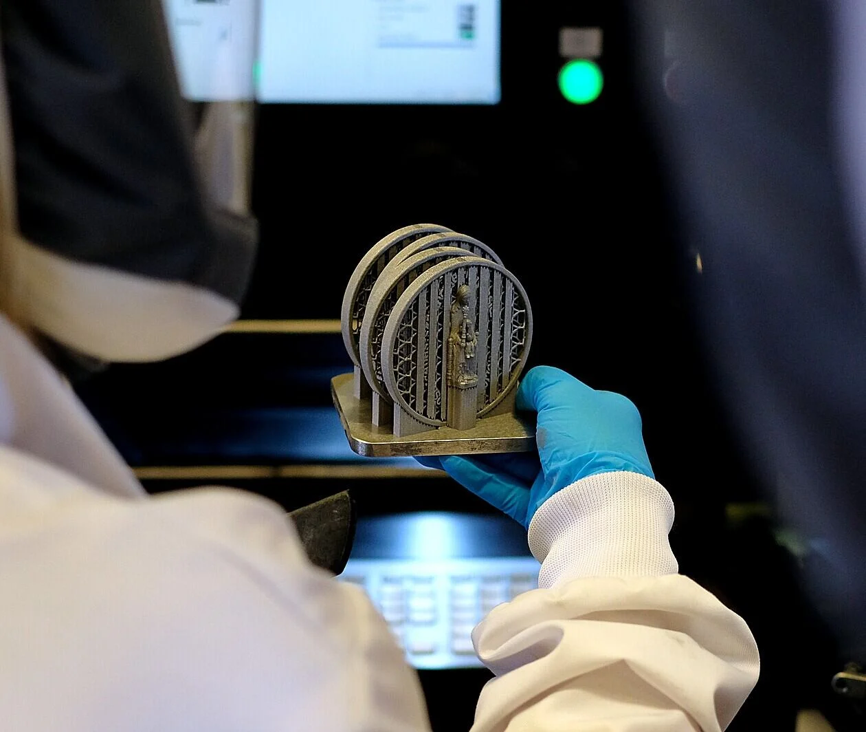 An additive manufacturing engineer holding a build plate with several Ti6Al4V demonstration parts which were manufactured using laser powder bed fusion technique