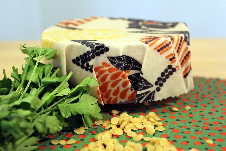 Picture of a dish covered in a beeswax wrap with some herbs and flakes of beeswax