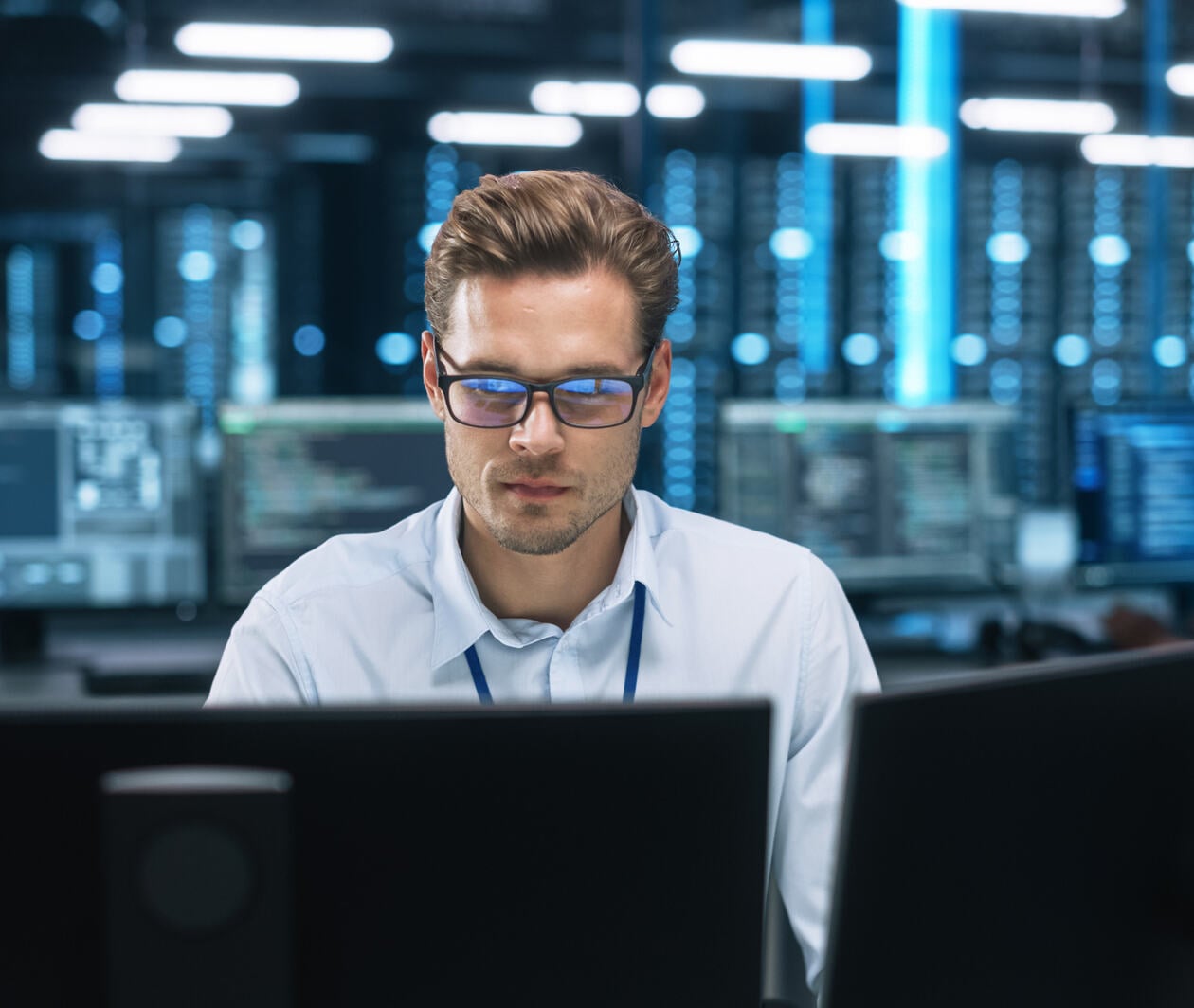 Man looking at double computer screens with more screens and desks behind him
