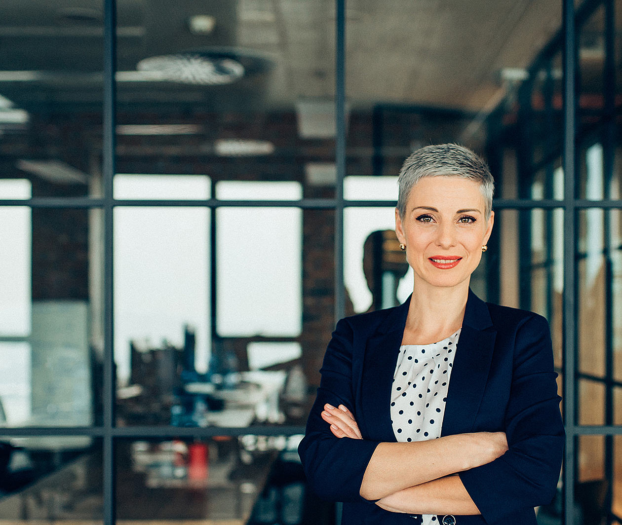 Business woman standing with her arms crossed in front of a glass paneled office.