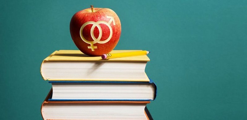 An apple with universal signs for male and female engraved in it, placed on top of a pile of books.