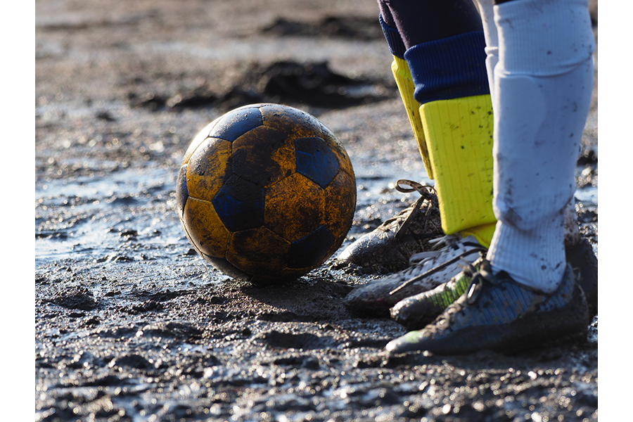 Soccer ball on a muddy field with the feet of two opposing players standing beside it