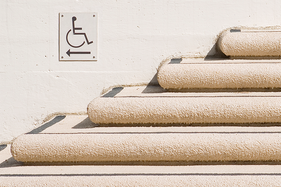 Sign on wall above steps pointing to wheel chair accessible ramp.