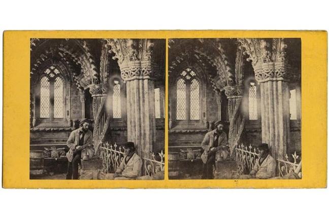 Interior of The Lady Chapel, Roslyn, showing two men, one standing and one seated, with intricate carved pillars behind.