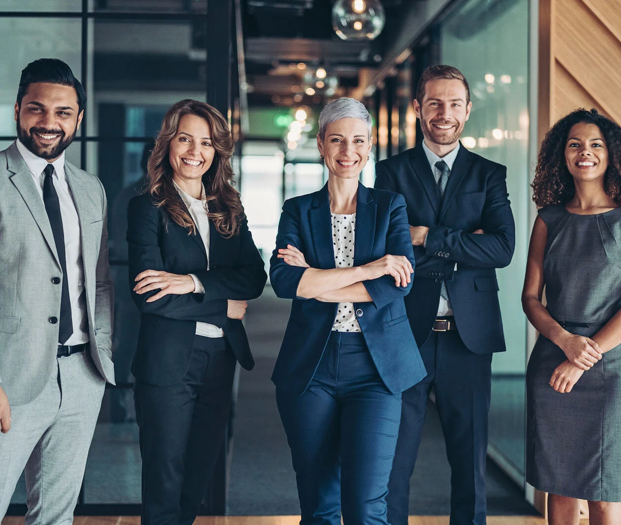 Multi-ethnic group of business persons standing side by side with 3 women and 2 men smiling to the camera which shows confidence.