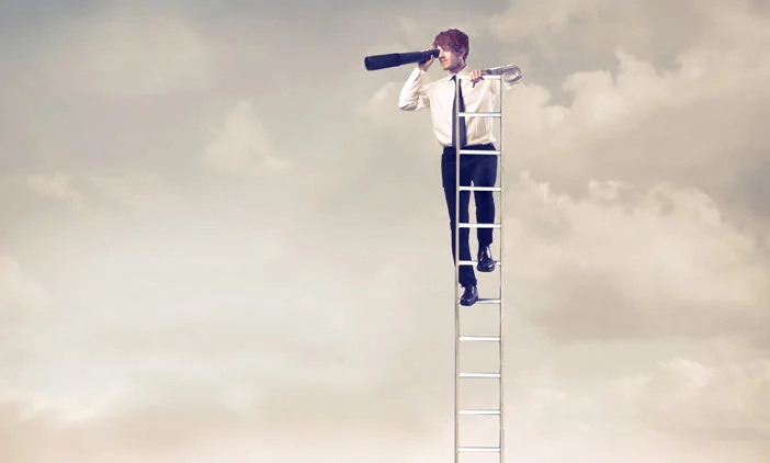 Young business man balanced on the top of a tall ladder. He is surrounded by clouds and is looking into the distance through a telescope.